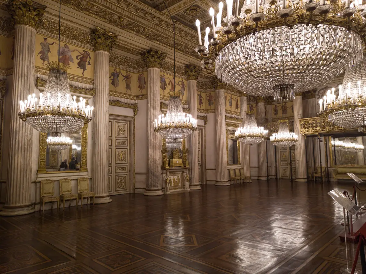 A ballroom of the Royal Palace with chandeliers and a painted ceiling.