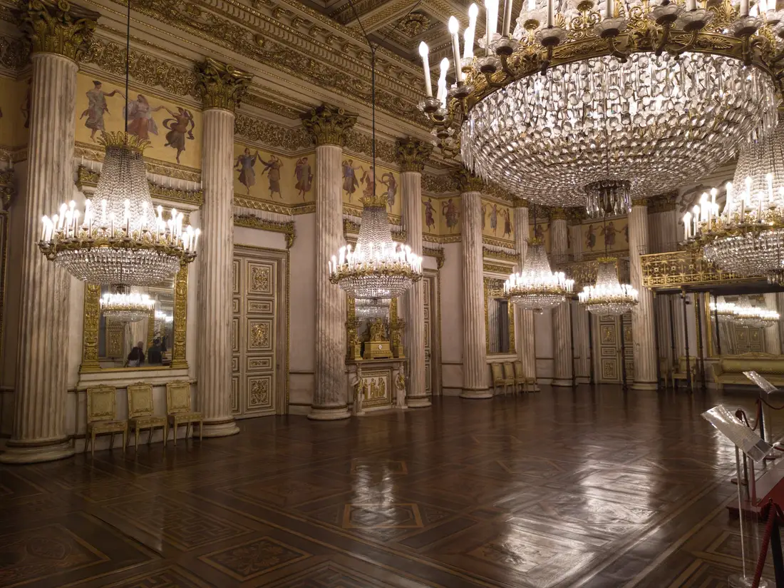 A ballroom of the Royal Palace with chandeliers and a painted ceiling.